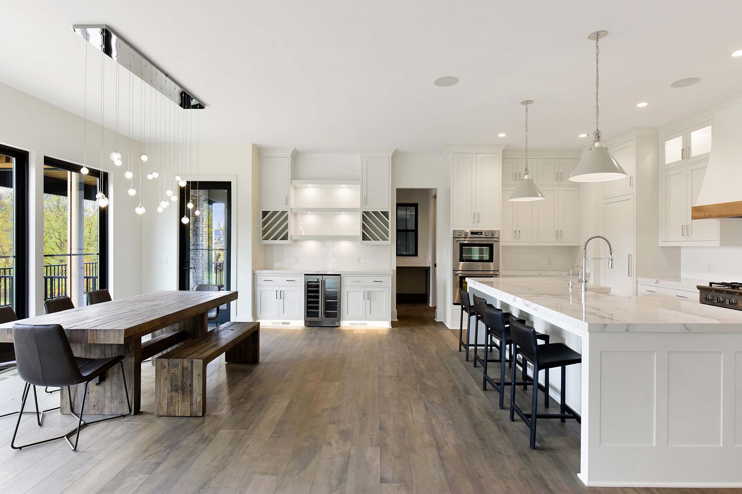 Contemporary kitchen with white island and dinette with hanging globe lights