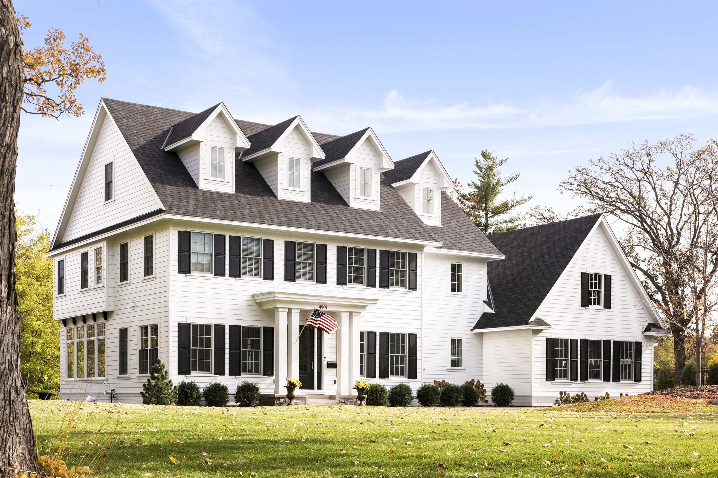 Colonial On The Creek Exterior Angle with white siding, black shutters, and American flag