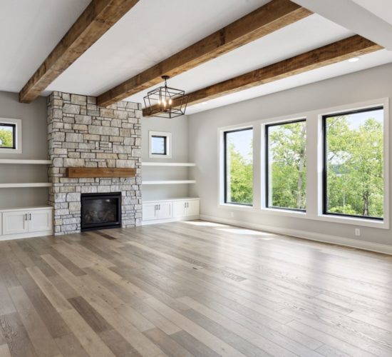 Great room with floor-to-ceiling stone fireplace, built-ins, floating shelves, and beamed ceiling