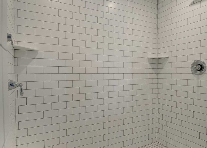 Shower with three shower heads and white subway tile interior